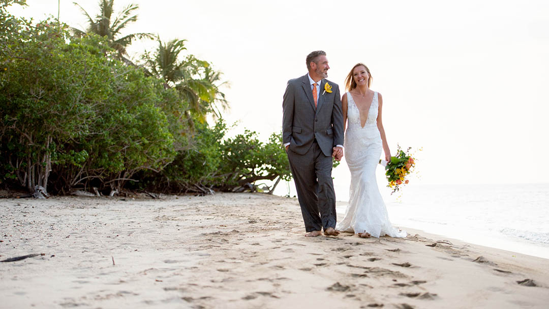 Married couple walking happily barefoot in the sand in St. Thomas.