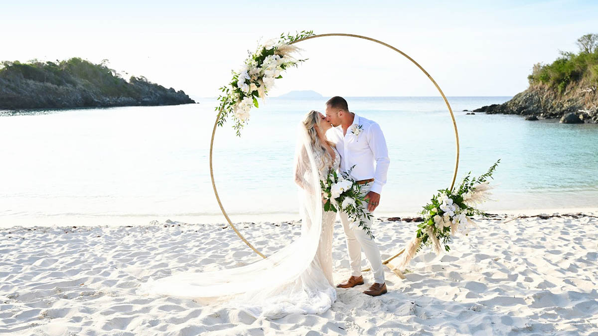 Married couple kissing barefoot on a palm tree overhanging the beautiful waters of St. Thomas.