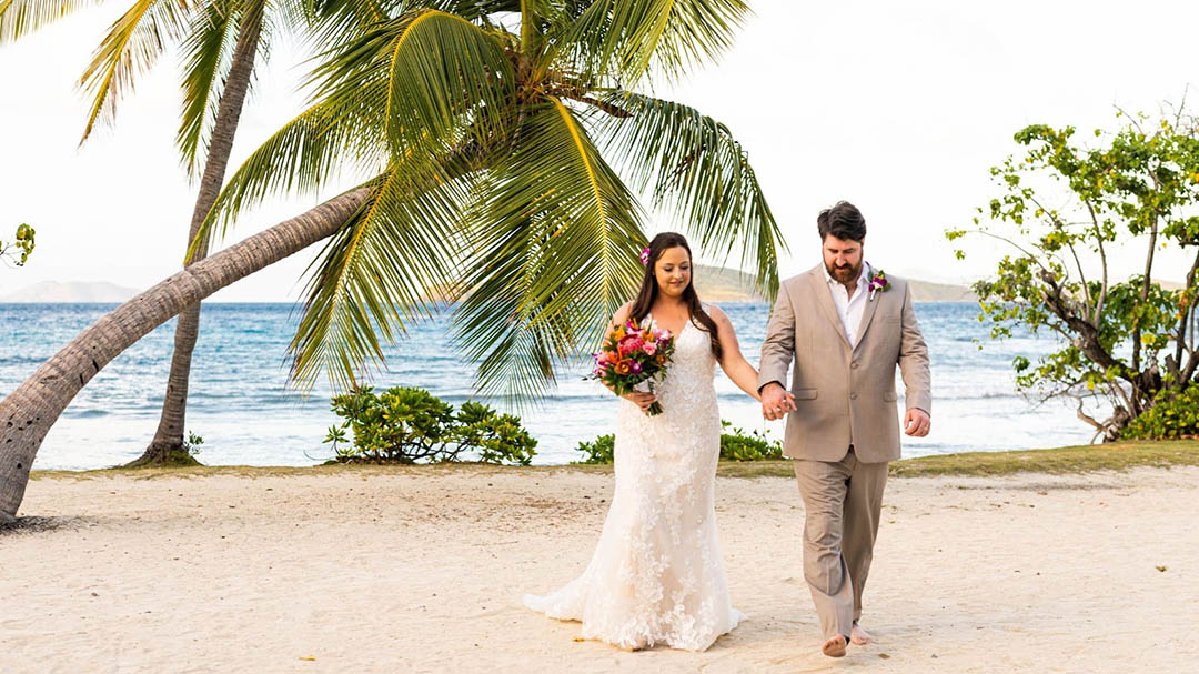 Married couple walking happily barefoot in the sand in St. Thomas.